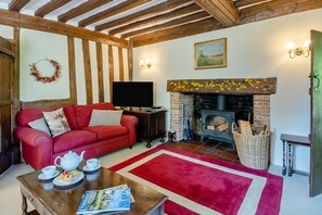 A cozy living room with a red sofa, a fireplace, a television, and a magazine on a coffee table. - 4 Bed in St. Nicholas South Elmham (oc-o32397) (All Saints South Elmham)