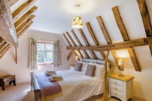 A bedroom with a sloped ceiling, a bed with pillows, a bedside table with a lamp, and a window with curtains. - 4 Bed in St. Nicholas South Elmham (oc-o32397) (All Saints South Elmham)