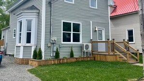 A two-story house with a red roof, a front porch with a wooden railing, and a small front yard with a gravel path and grass. - Downtown Oasis Moncton (Moncton)