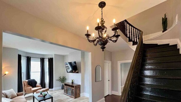 A spacious living room with a staircase, a chandelier, and a flat-screen TV. - Downtown Oasis Moncton (Moncton)
