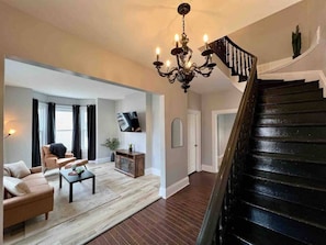 A spacious living room with a staircase, a chandelier, and a flat-screen TV. - Downtown Oasis Moncton (Moncton)