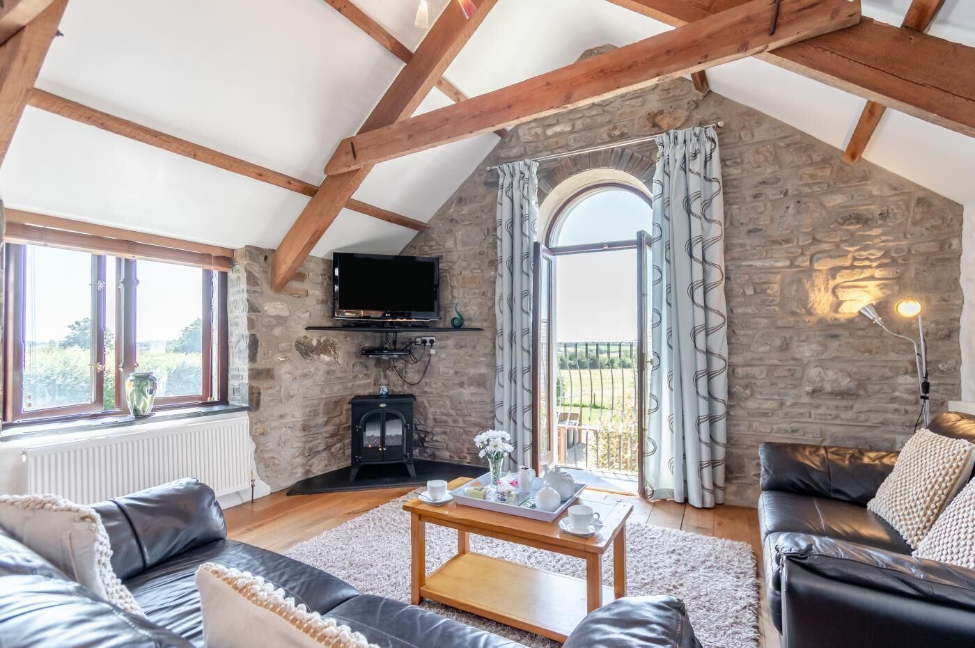 A cozy living room with a stone fireplace, a television, and a large window with curtains.