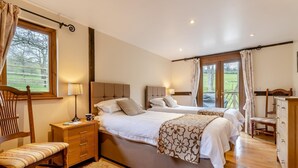 Un dormitorio con dos camas, una silla de madera, una mesita de noche, un aparador y una ventana con cortinas.