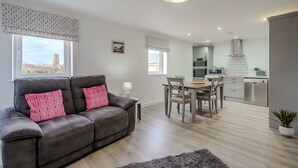 Ein modernes Wohnzimmer mit Sofa, Esstisch und einer Küche im Hintergrund.