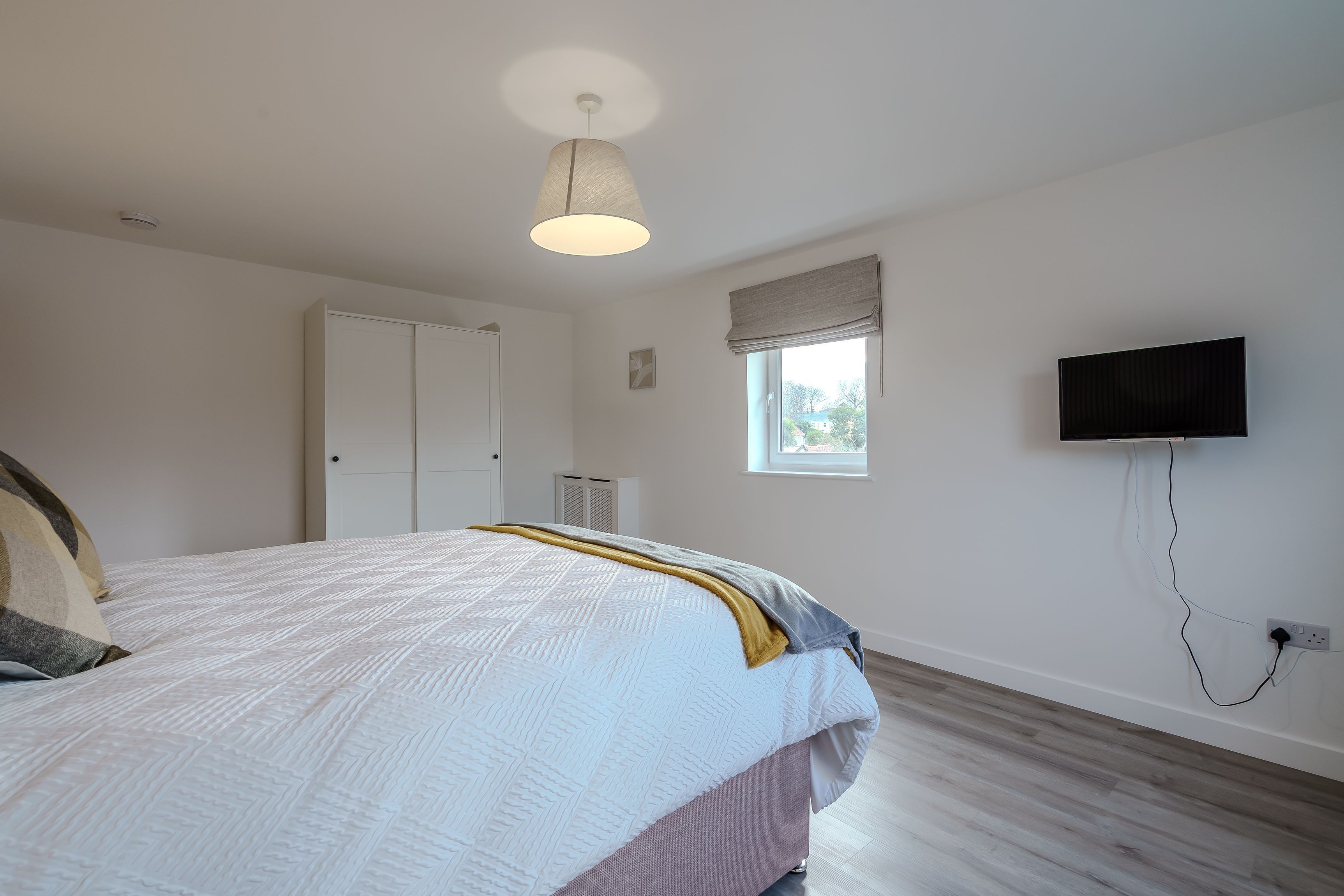 Une chambre à coucher avec un lit, un luminaire au plafond, une fenêtre, un téléviseur et une armoire.