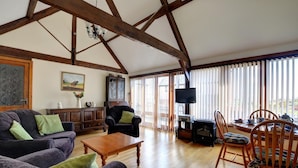 Ein geräumiges Wohnzimmer mit Holzbalken, einem Kamin, einem Fernseher und einem Essbereich mit traditionellen Möbeln.