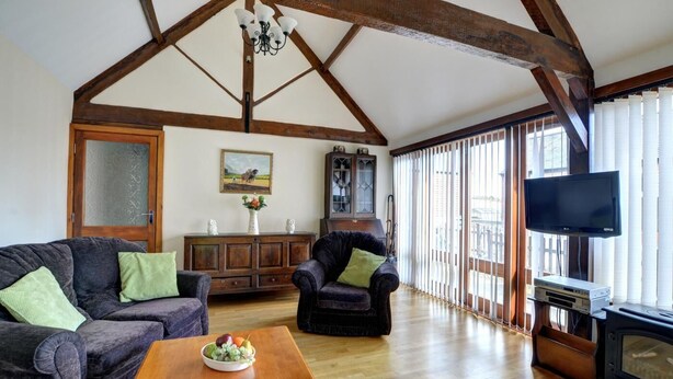 Ein geräumiges Wohnzimmer mit Holzboden, Kamin, Fernseher und großem Fenster mit Jalousien.