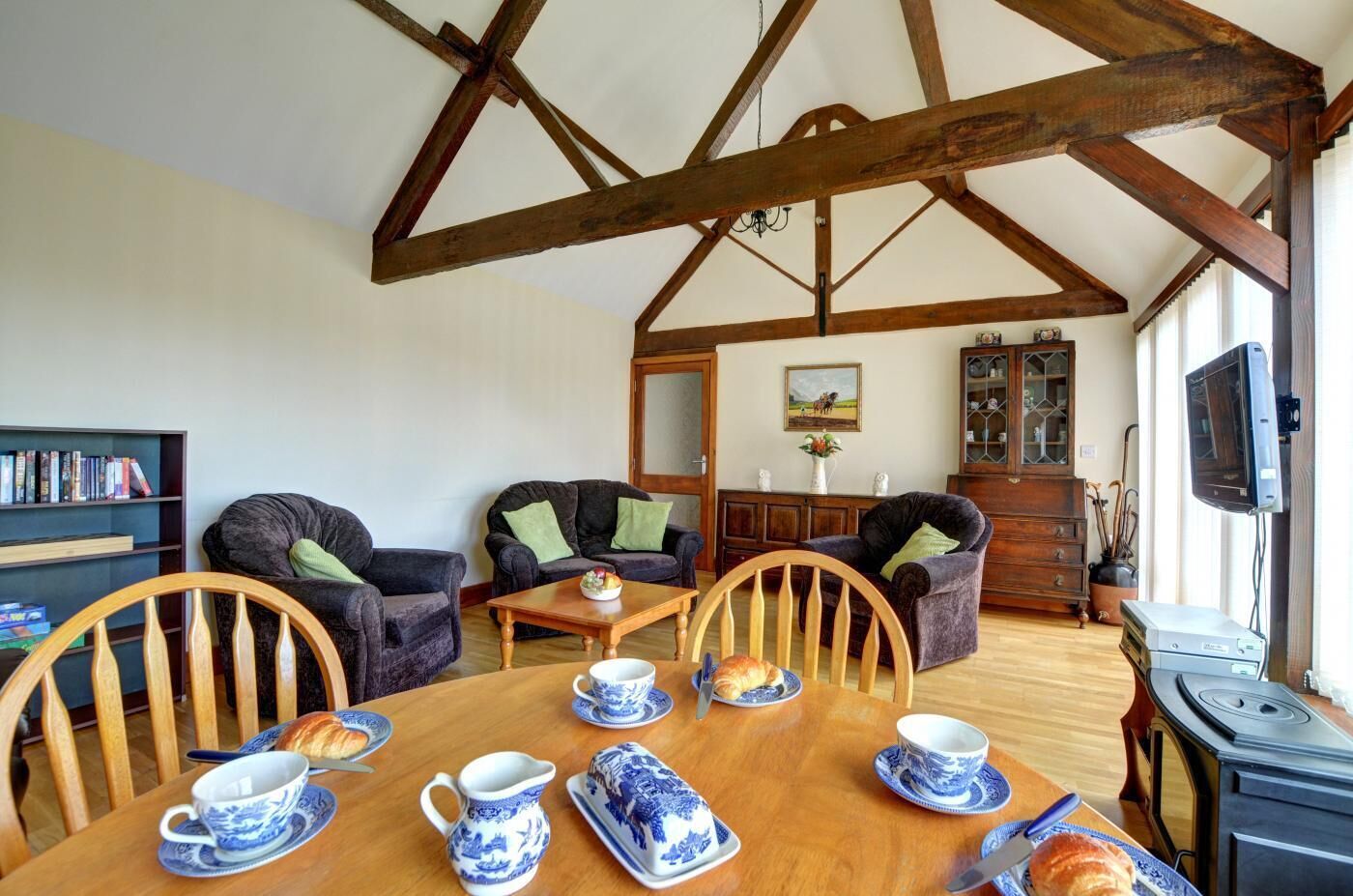 Un salon chaleureux avec de hauts plafonds, des poutres apparentes, une table à manger dressée avec de la vaisselle bleue et blanche, et des sièges confortables.