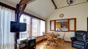 Ein Wohnzimmer mit Fernseher, einem Holzespeisetisch, Stühlen, einem schwarzen Ledersessel und einer Küchenzeile mit Schränken und einer Uhr.