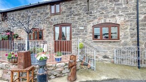 Un edificio in pietra con un portico in legno, piante in vaso e un cancello in metallo.