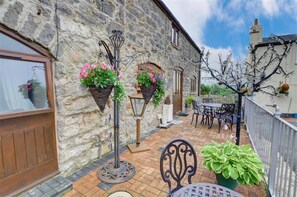 A stone building with a patio area featuring a table and chairs, a hanging light fixture, and potted plants. - 2 Bed in Abergele (oc-wag501) (Dolwen)