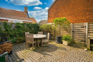 Eine Terrasse mit rundem Tisch und Stühlen, umgeben von Topfpflanzen und einer Backsteinmauer.