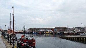 A harbor with boats docked, a pier with a railing, and a building in the background. - 2 Bed in Tankerness (oc-q32730) (Tankerness)