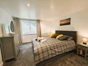 Une chambre à coucher comprenant un lit, une table de chevet, une commode, une fenêtre avec des rideaux et un tableau accroché au mur.