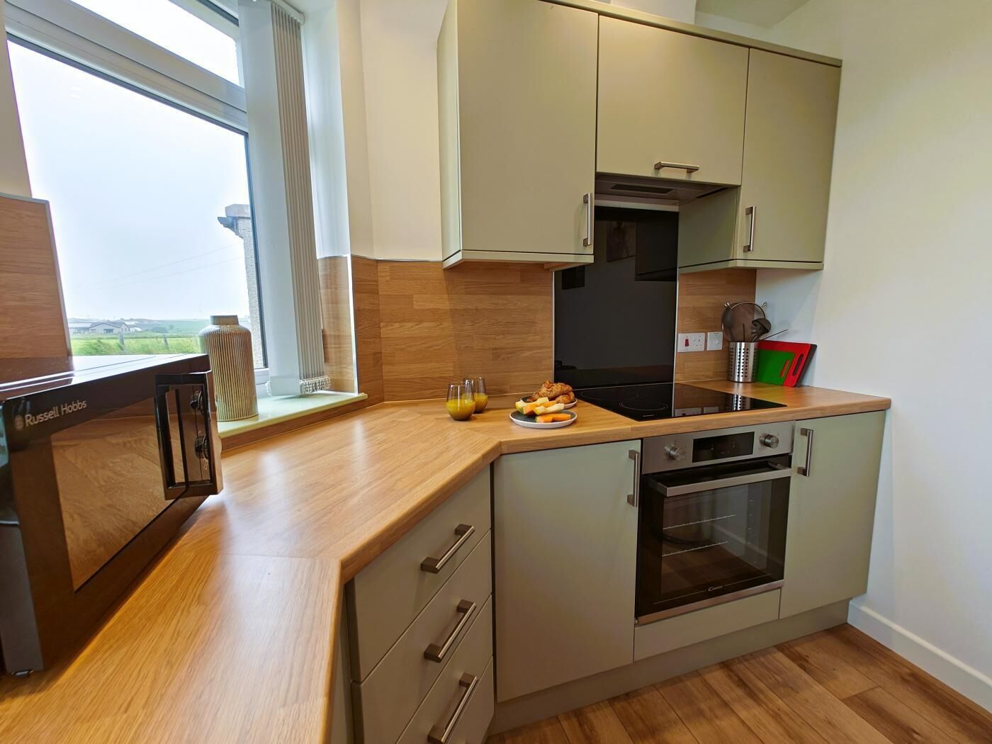 Una cucina compatta con un piano di lavoro in legno, forno integrato e finestra con vista sulla campagna.