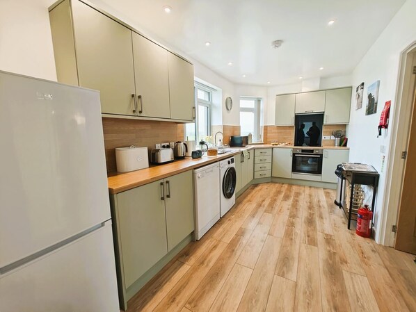 Une cuisine moderne avec un revêtement de sol en bois clair, des appareils électroménagers intégrés et un grand plan de travail.