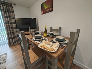 Une table à manger dressée avec des assiettes, des verres, une bouteille de vin, du fromage et des crackers.
