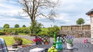Un espace extérieur aménagé pour les repas, avec une table, des chaises et une vue sur un jardin et un mur en pierre.