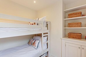 Una cama litera con una cama inferior y una individual, un estante con cestas y un armario con cajones.