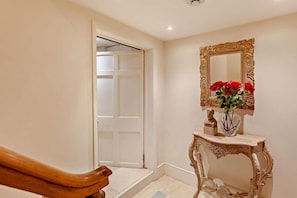 A hallway with a white door, a mirror with a gold frame, and a vase with red flowers on a console table. - 4 Bed in Widcombe (oc-bhr13) (Bath)