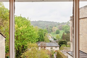 A view from a window overlooking a rural landscape with houses, trees, and a hill in the distance.