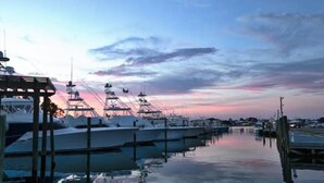 A marina with several boats docked, a wooden pier, and a calm water surface reflecting the sky. - Luxury Pet-friendly Home With Game Room & Community Pool (Orange Beach)
