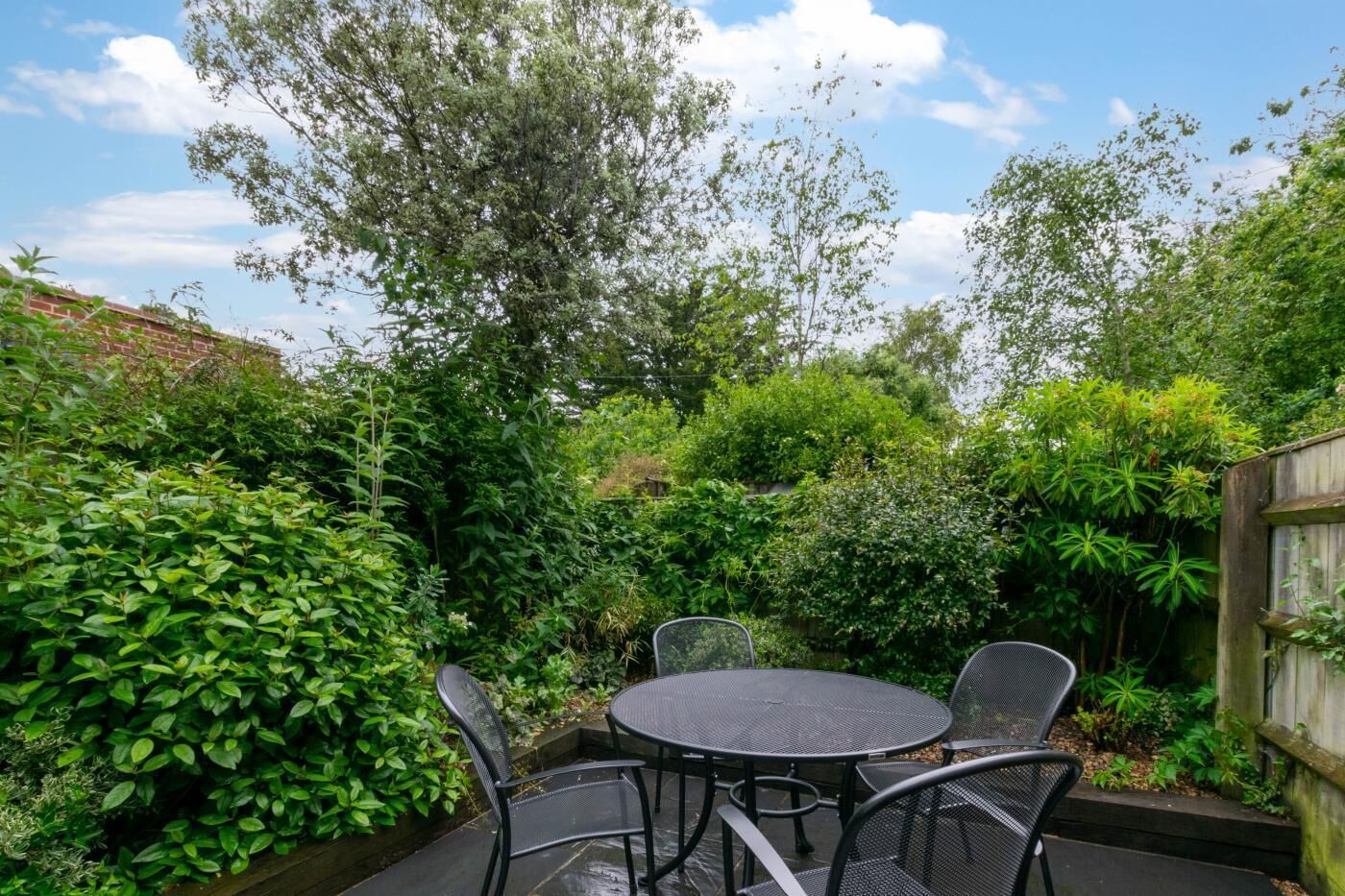 A round metal table with four chairs in a lush garden setting.