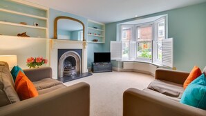 A living room with a fireplace, a television, and a bay window with shutters. - 2 Bed in Walberswick (oc-hhock) (Walberswick)
