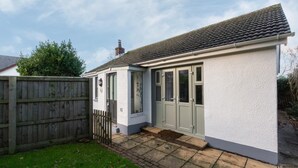 A single-story house with a tiled roof, a front door with glass panels, and a small front yard with a wooden fence.