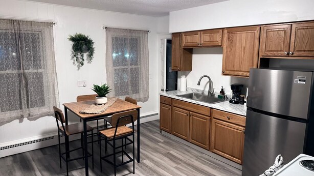 A modern kitchen with wooden cabinets, a stainless steel refrigerator, a sink, and a dining table with chairs. - 3BR Hamden Stay Near Yale, Southern, Quinnipiac & New Haven (Hamden)