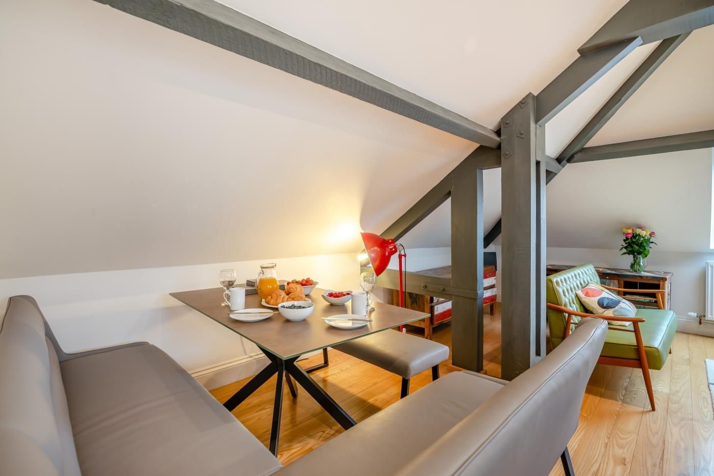 A modern loft bedroom with a dining area, a green sofa, and a red lamp.