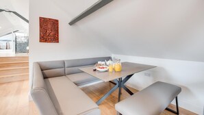 Un loft moderno con zona de comedor, una mesa de vidrio, asientos con cojines grises y un elemento decorativo en la pared.