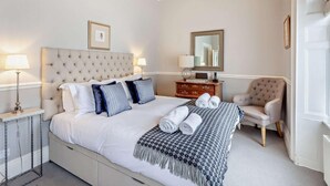 A neatly arranged bedroom with a large bed, bedside tables, a chair, a dresser, and a mirror. - 2 Bed in Bath (oc-bhr6) (Bath)