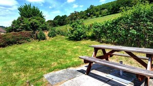 Une table de pique-nique se trouve dans une zone herbeuse, avec des arbres et des collines en arrière-plan.