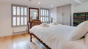 Quarto com cama, cómoda de madeira, radiador e janela com persianas.