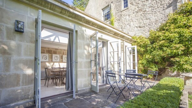 A stone building with a patio area featuring a table and chairs, and a door leading to an interior space with framed artwork. - 7 Bed in Combe Hay (oc-bhr21) (Combe Hay)