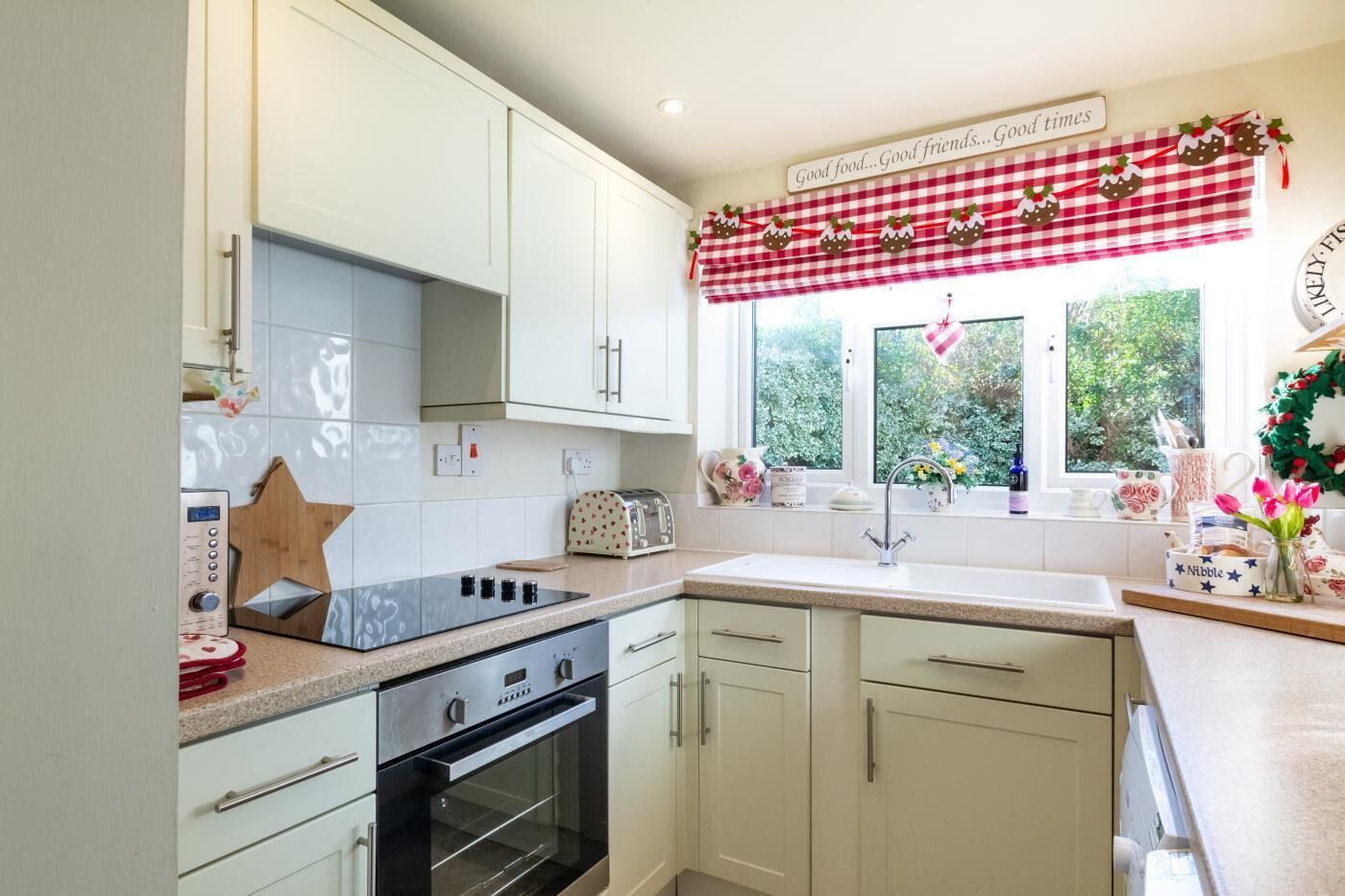 A kitchen with white cabinets, a black oven, a window with a checkered valance, and a sign above the window.
