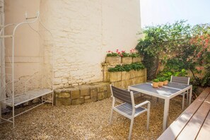 A patio with a table and chairs, a metal chair, a stone wall with plants, and a wooden bench. - 3 Bed in Bath (oc-bhr53) (Bath)