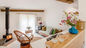 Een gezellige woonkamer met een open haard, een houten plafond, een eethoek met tafel en stoelen, en een keuken met een fornuis.
