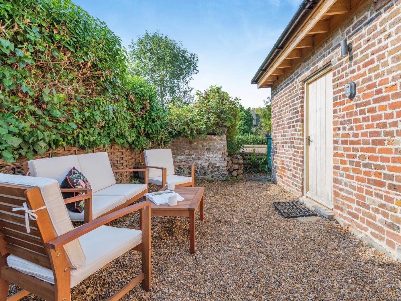 A patio with a wooden table and two chairs, a brick wall, and a door.