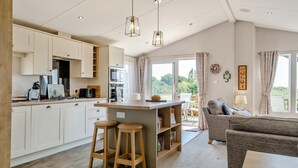 A modern kitchen with white cabinets, a central island with stools, and a dining area with a sofa and table. - 2 Bed in Upton (oc-h32761) (Ryde)