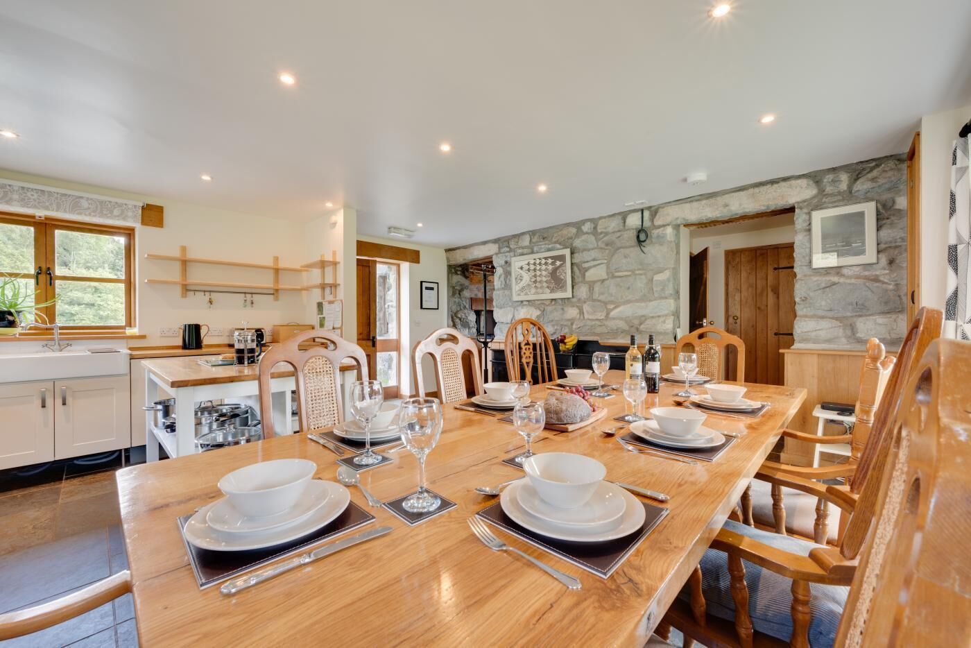 A dining area with a long wooden table set for a meal, surrounded by stone walls and wooden furniture.