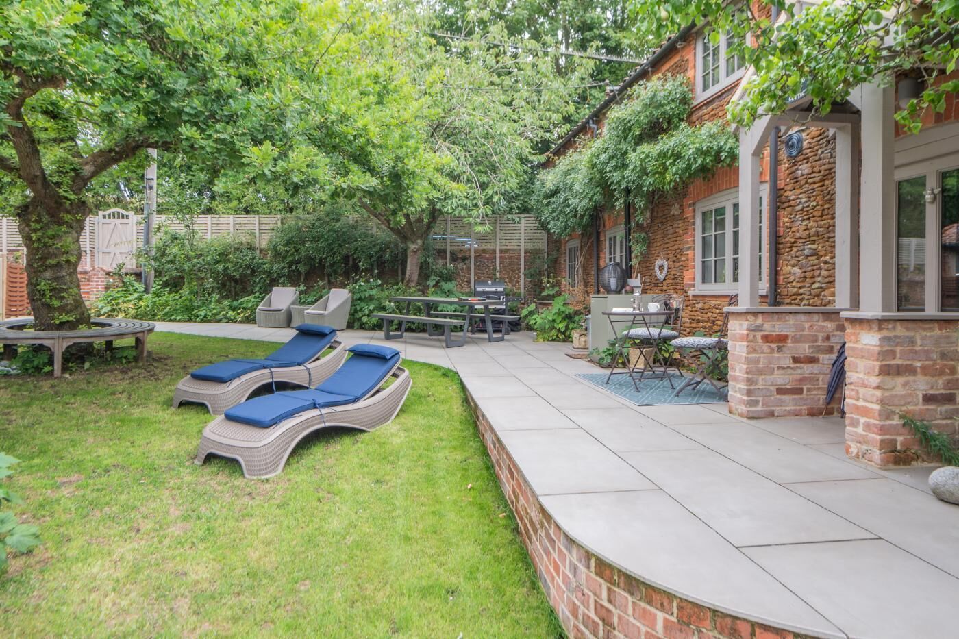 Un patio trasero con mobiliario de exterior, sillones de descanso, una parrilla y un muro de piedra.