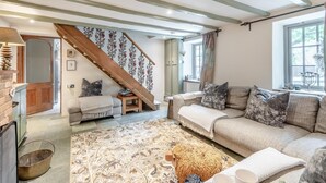 A cozy living room with a sofa, a patterned rug, and a staircase with floral wallpaper. - 3 Bed in Sedgeford (oc-s32725) (Sedgeford)
