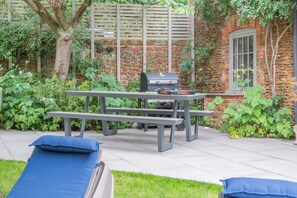 Une terrasse extérieure équipée d’un barbecue, d’une table de pique-nique et de chaises longues.