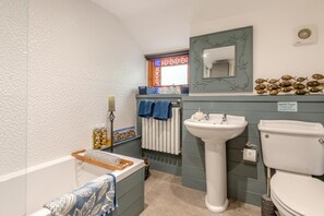 Une salle de bain avec une baignoire, un lavabo et des toilettes. Il y a une fenêtre avec un cadre décoratif et un miroir au-dessus du lavabo.