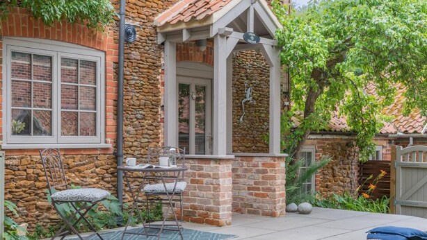 A stone house with a patio, a small table with chairs, and a garden. - 3 Bed in Sedgeford (oc-s32725) (Sedgeford)