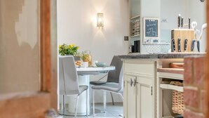 A modern kitchen with a dining area, featuring a white table, grey chairs, and a small plant. - 3 Bed in Sedgeford (oc-s32725) (Sedgeford)