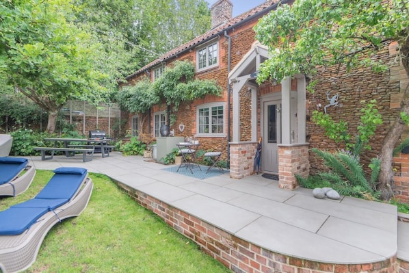 Une maison avec une façade en pierre, un patio doté de chaises longues et une petite piscine.