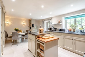 Une cuisine moderne dotée d’un îlot central, d’un coin repas avec une table et des chaises, et d’une fenêtre qui laisse entrer la lumière naturelle.